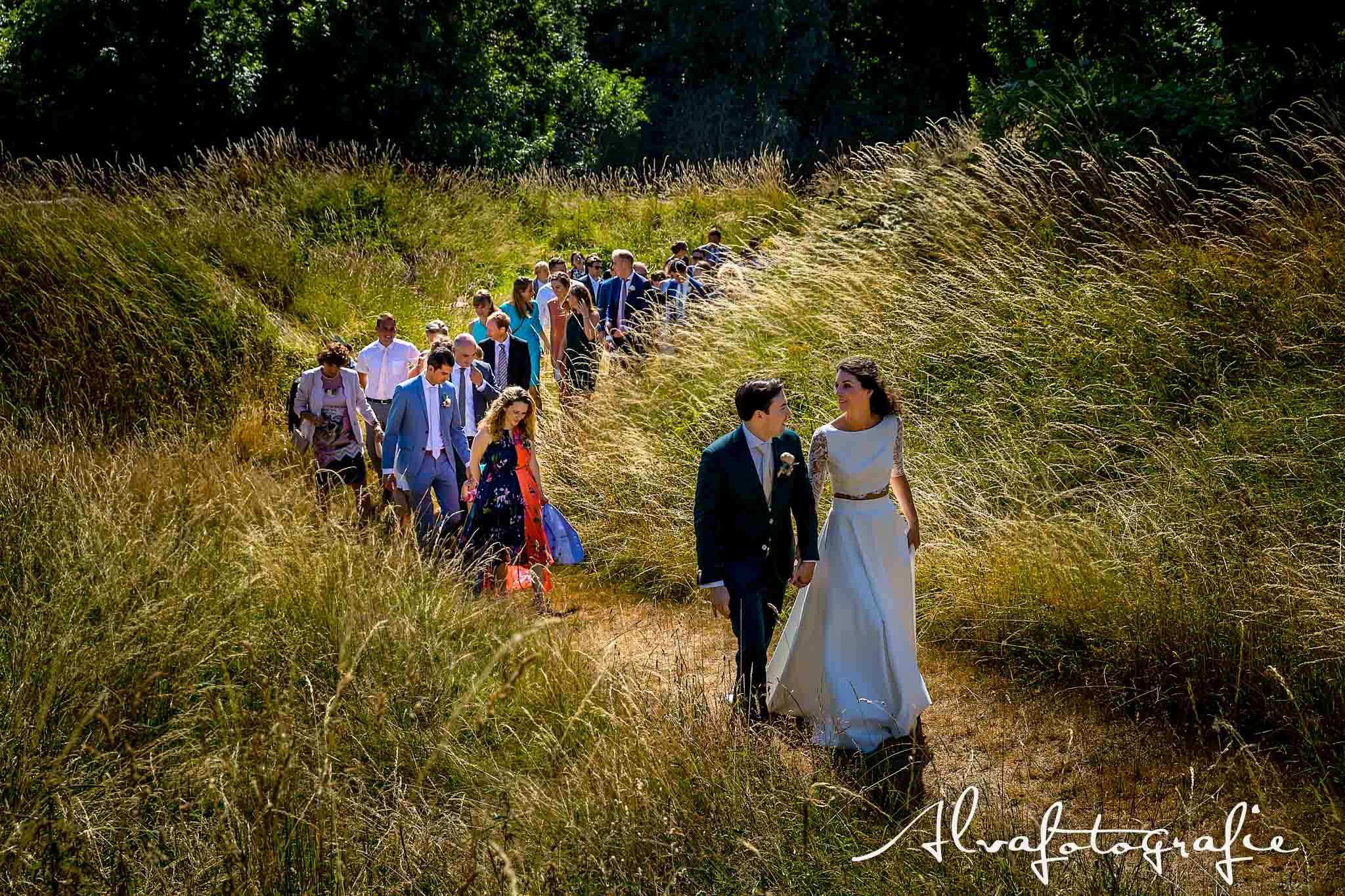 Bruiloft Maren en Tim Alvafotografie bruidspaar loopt heuvel op met gasten Paviljoen Puur